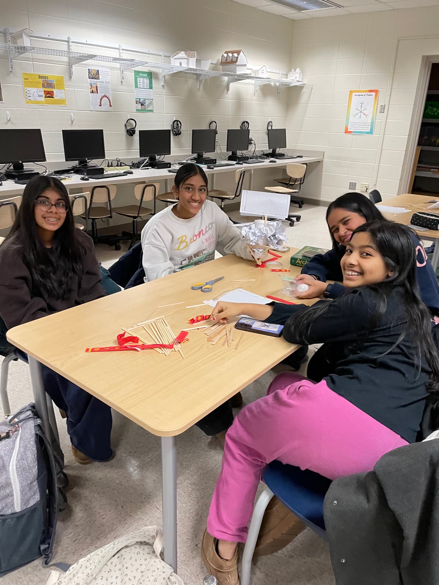 Four students building a structure from craft sticks and tape at a Girls in STEM meeting
