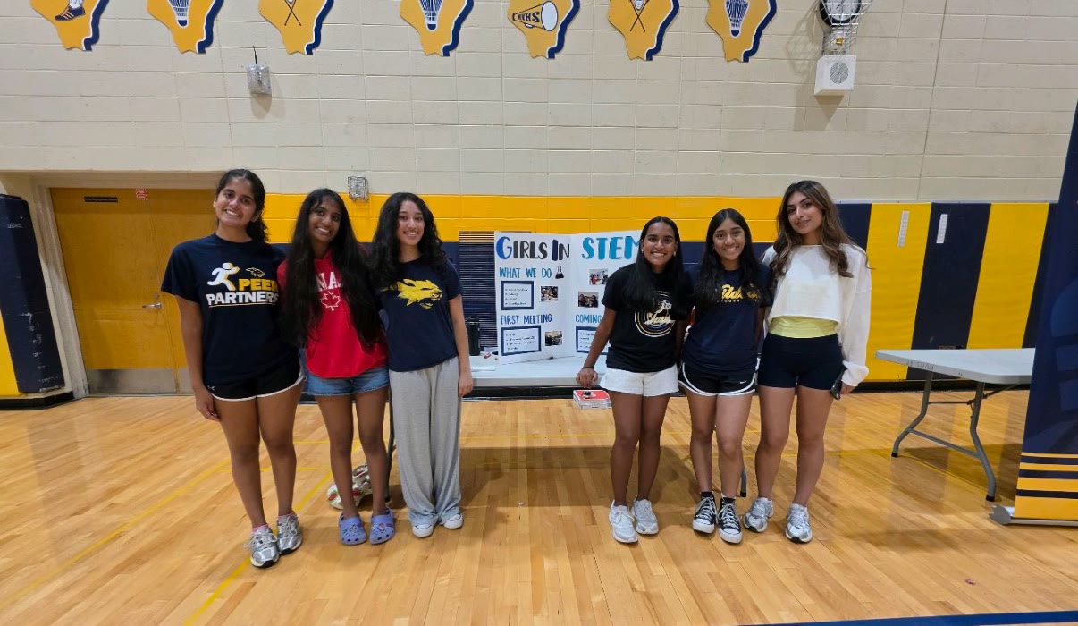Six Girls in STEM members beside the club’s poster in the school gym